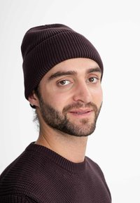 Dark purple ribbed beanie worn with a textured dark sweater. Beanie fits snugly, showing horizontal and vertical knit patterns.