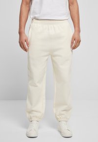 Pantaloni de trening de culoare crem, cu un talie elastică și glezne strânse, având buzunare laterale și o textură netedă. Asociați cu adidași albi.