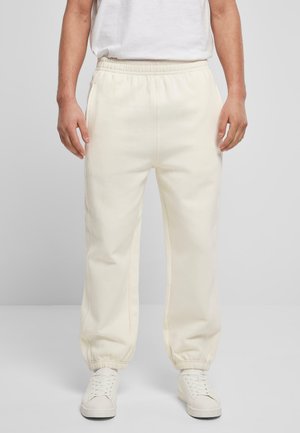 Cream-colored sweatpants with an elastic waistband and cuffed ankles, featuring side pockets and a smooth texture. Paired with white sneakers.