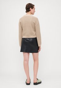 Beige strikket genser med cropped design, kombinert med et svart skinn miniskjørt. Enkle grønne slip-on sko fullfører antrekket.