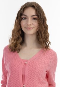 Rosa stickad cardigan med v-ringning, har ett texturerat mönster, knappstängning och långa ärmar. Bärs över en matchande linne.