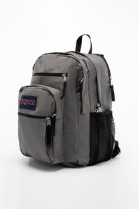 Sac à dos en nylon gris avec plusieurs poches zippées, poche latérale en mesh, bretelles rembourrées et une poignée supérieure. Affiche le logo Jansport à l'avant.