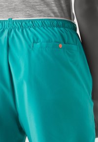 Tyrkysové šortky s elastickým pasem, se zadní kapsou s oranžovým knoflíkem. Hladká, lehká tkanina s matným povrchem.