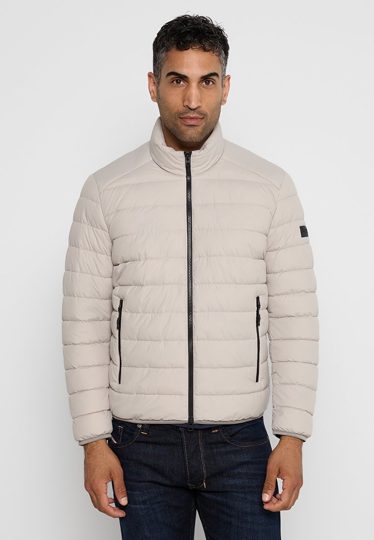 Helle beige Daunenjacke mit hohem Kragen, horizontalem Steppmuster, schwarzem Reißverschluss und Seitentaschen; glatte Textur.
