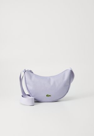 Sac à bandoulière en tissu lilas avec une forme arrondie, fermeture éclair et un logo crocodile brodé en vert. Bandoulière réglable pour un port en travers.