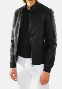 Giacca bomber nera in pelle con collo alto, chiusura con zip e polsini a costine. Il materiale ha una finitura liscia e un design aderente.