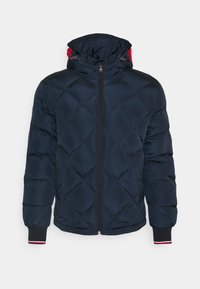 Marinblå vadderad jacka med quiltat mönster, framzipper, justerbar huva och ribbade ärmslut med vita och röda ränder.