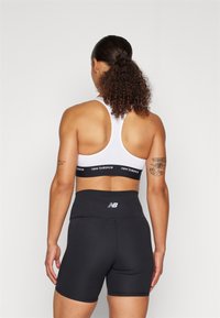 Juoda sportinė šortai su plačiu, aukštu juosmeniu, derinami su balta sportine liemene, turinčia juodą 'New Balance' logotipo juostą.