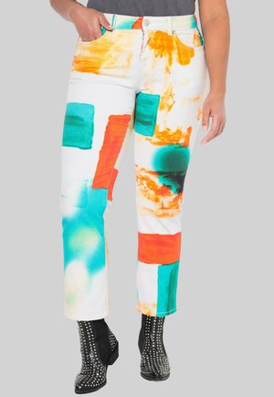 Pantalones vaqueros blancos con patrones abstractos audaces en naranja, teal y verde. Tienen un diseño de pierna recta y se combinan con botas negras con tachuelas.