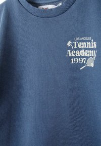 Felpa blu con collo a giro, caratterizzata da testo bianco che recita "LOS ANGELES Tennis Academy 1997" e una grafica di una racchetta da tennis.