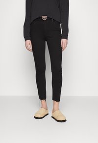 Černé úzké džíny s roztrženými lemy, spárované s béžovými nazouvacími botami. Model nosí černou mikinu a dekorativní opasek.