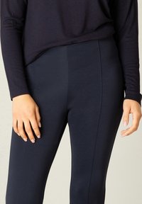 Marineblauwe leggings van een soepel, rekbaar materiaal met een slim fit ontwerp. Verticale naden zorgen voor een gestroomlijnd uiterlijk. Langsleeve top deels zichtbaar.