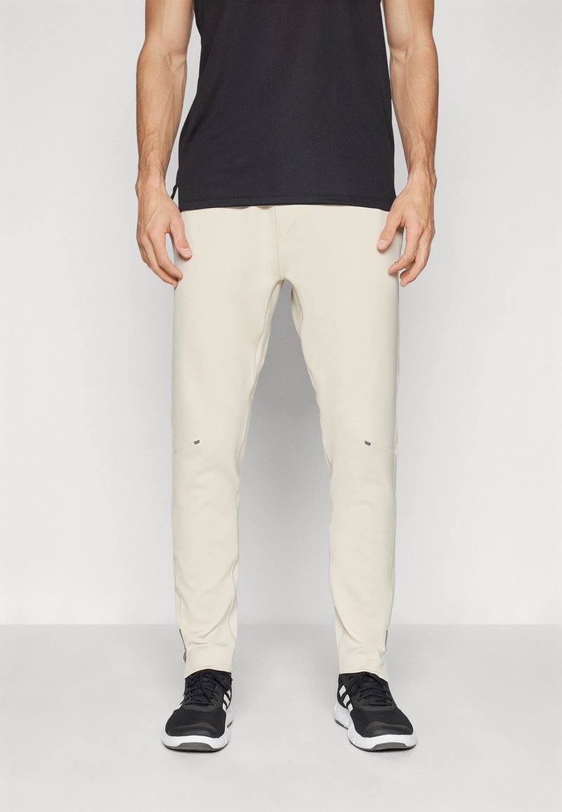Beige sweatpants with a slim fit, featuring a textured surface, subtle side pockets, and contrasting dark accents; paired with black shoes.