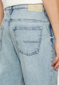 Lichtblauwe denim jeans met een klassieke pasvorm, voorzien van een leren merkpatch bij de taille en twee achterzakken met subtiele stikseldetails.