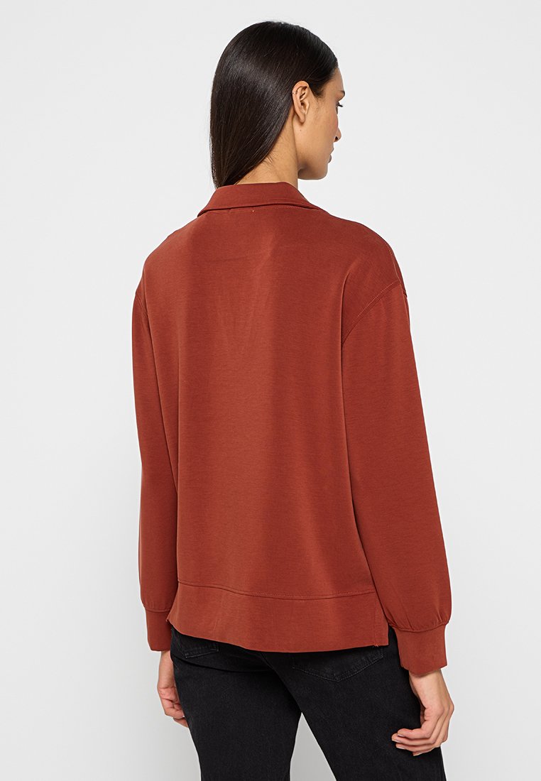 Sweatshirt surdimensionné couleur rouille avec col, manches longues, poignets côtelés et ourlet droit. Tissu lisse avec des détails de couture subtils.