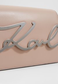 Różowa torebka skórzana z wyraźnym srebrnym logo. Gładka tekstura, elegancki, minimalistyczny design i ukryte szwy.