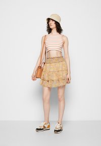 Top cropped às riscas, saia mini de camadas florais, chapéu de balde bege, mala de ombro castanha e ténis multicoloridos; conjunto casual de verão.