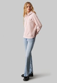 Lys rosa hettegenser med en frontal kengurulomme og snorhette, kombinert med lyseblå slengjeans og svarte platå sko.