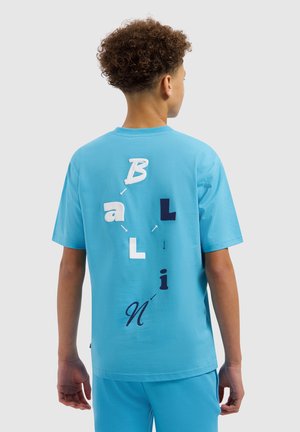 Jongen met krullend haar die een lichtblauw T-shirt en korte broek draagt, met op zijn rug de tekst "Ballin" in gemengde lettertypen en kleuren met pijlen.