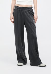 Szare, luźne dresy z elastycznym paskiem w talii i detalami wzdłuż szwów bocznych. Zawierają logo na lewej udzie. Miękki materiał tekstylny.