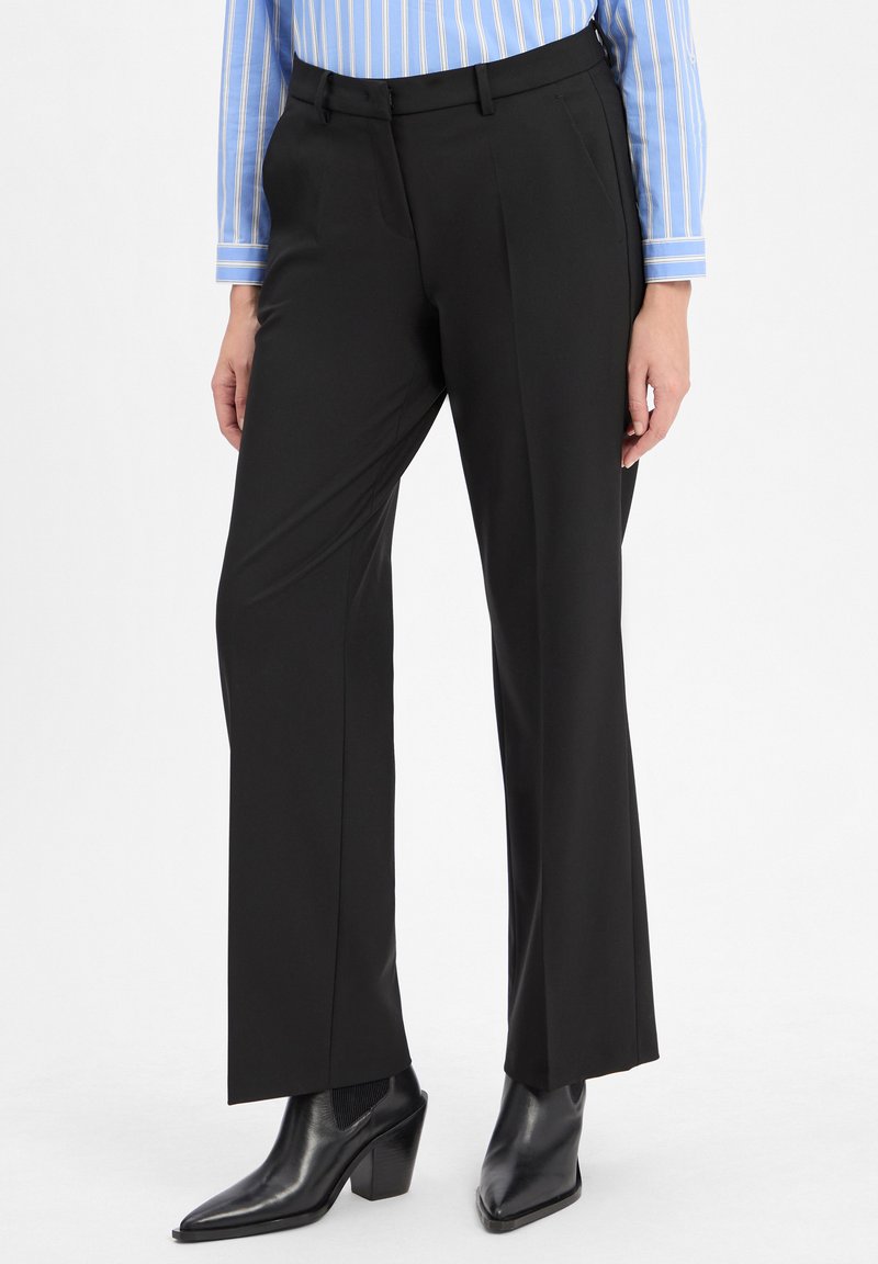 Zwarte op maat gemaakte pantalon met een rechte pijpdesign, gemaakt van soepel stof. Voorzien van riemlussen en een persplooi; gedragen met zwarte hakboots.