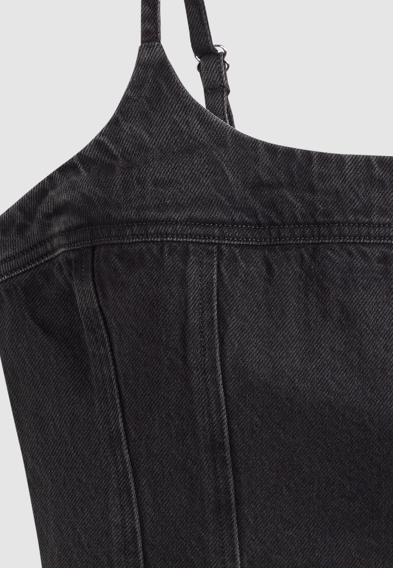 Gros plan d'une robe en denim noir avec des bretelles fines réglables et des détails de coutures visibles sur un fond clair.