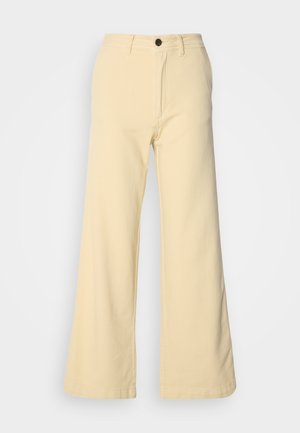 Calças de perna larga em amarelo claro, feitas de um tecido misto de algodão. Apresentam um fecho frontal com botão, passantes para cinto e dois bolsos laterais.