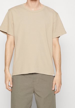 Beżowa, prążkowana koszulka z okrągłym dekoltem i krótkimi rękawami, wykonana z miękkiej bawełny, zestawiona z szarymi spodniami.