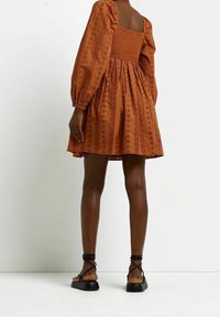 Brun, kort klänning med fyrkantig halsringning, puffärmar och en samlad midja, med strukturerade broderimönster över hela.