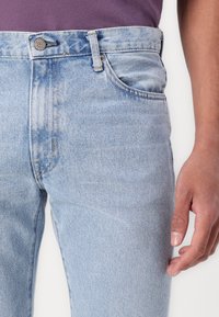 Light blue denim jeans featuring a slim fit, five-pocket design, and a button fly. The fabric has a subtle texture and slight fading.