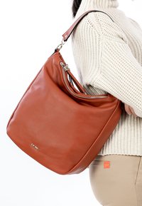 Große, rostfarbene Ledertasche mit glatter Textur, ausgestattet mit einem Reißverschluss und einem verstellbaren Riemen.