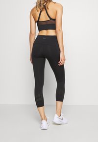 Czarne legginsy sportowe z siateczkowymi detalami i perforacjami na łydkach. W zestawie z czarnym biustonoszem sportowym. Widoczne białe sneakersy.