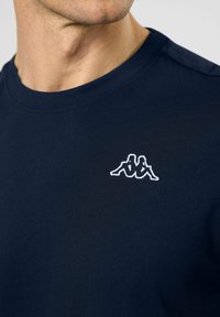 Temno moder kratkoročni majico s krožnim ovratnikom in vezenim belim logotipom Kappa na prsih. Gladko bombažno blago, prilegajoča zasnova.