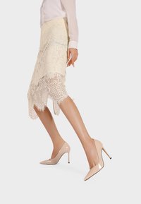 Décolleté in pelle verniciata beige con punta affusolata e sottile tacco a stiletto, abbinati a una gonna in pizzo con intricati motivi floreali.