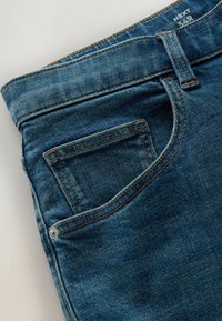 Jean en denim bleu montrant une poche avant, une boucle de ceinture, un rivet et une étiquette de taille "NEXT 34R" sur la ceinture.