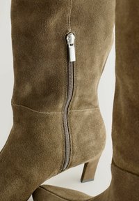 Botas de tacón alto de ante marrón con cremallera lateral y tacón rectangular. Textura suave con un sutil detalle de costura.