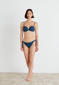 Pusmēnešu zils bikini komplekts ar polsterētu krūšturi ar regulējamiem siksniņām un atbilstīgiem priekškā pamatiem, izgatavots no gludas auduma ar minimālu apdari.