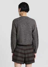 Brown cable-knit sweater with a cropped, rounded hem and oversized sleeves, paired with checkered brown shorts featuring vertical stripes.