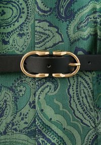 Cinturón de cuero negro con una hebilla ovalada de tono dorado sobre una tela verde con un patrón de paisley en verdes más oscuros y azul marino.