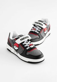 Schwarze synthetische Turnschuhe mit weißen und roten Akzenten, die ein Poké Ball-Design aufweisen, einen Klettverschlussriemen und eine strukturierte Sohle für besseren Halt haben. Weiße Schnürsenkel sind inklusive.