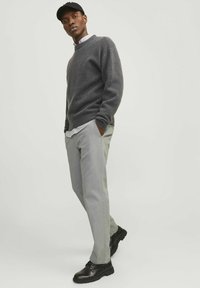 Kohlenstofffarbener Wollpullover, hellgraue Chinos und schwarze Schuhe. Der Pullover hat einen runden Ausschnitt und gerippte Bündchen; die Chinos sind gerade geschnitten.