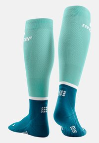 Turquoise voetbal sokken met een gestructureerd patroon, witte accenten aan de bovenkant en enkel, en een donkerblauwe voetsectie met gripdetails.