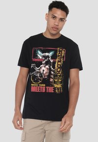 Schwarzes T-Shirt mit einem Grafikdruck eines robotischen Dinosauriers und dem Text "Grimlock" in Gelb und Pink. Kurze Ärmel und lockere Passform.