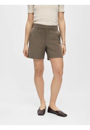 Personne portant un short taupe sur mesure au genou, un top beige à manches courtes, des chaussures plates pointues marron et un bracelet fin en argent au poignet gauche.