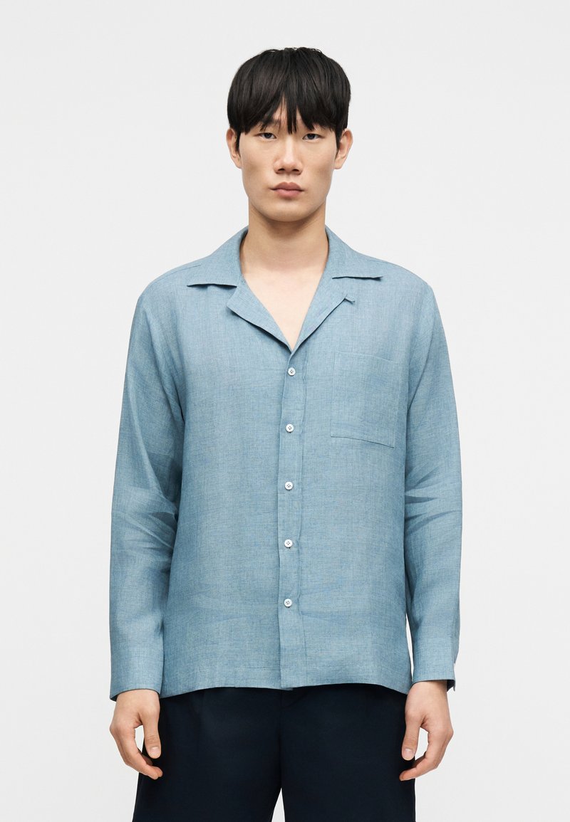 Ανοιχτό μπλε, μακρυμάνικο πουκάμισο με γιακά, μπροστινή τσέπη και κλείσιμο με κουμπιά. Κατασκευασμένο από υλικό με υφή και χαλαρή γραμμή.