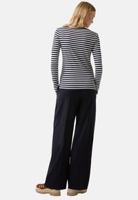 Woman with long blonde hair wearing a black and white striped long-sleeve top, wide-leg black pants, and brown shoes, facing away.