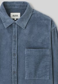 Chemise en velours côtelé bleu avec un devant boutonné, un col pointu et une poche poitrine, présentant une texture rayée verticale sur l'ensemble.