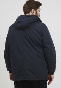 Mørkeblå hettejakke med glatt, vannavstøtende stoff, elastiske mansjetter og et midtlange design med en litt innsnevret midje.