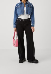 Denim cropattu takki, jossa on niititetyt hartiaakselit, yhdistettynä mustiin leveälahkeisiin housuihin ja paksupohjaisiin mustiin kenkiin. Mukana vaaleanpunainen käsilaukku.