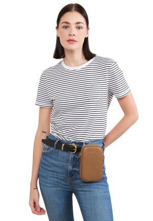 Kobieta ubrana w biało-czarną pasiastą koszulkę, niebieskie dżinsy oraz czarny pasek z przymocowaną brązową skórzaną saszetką.